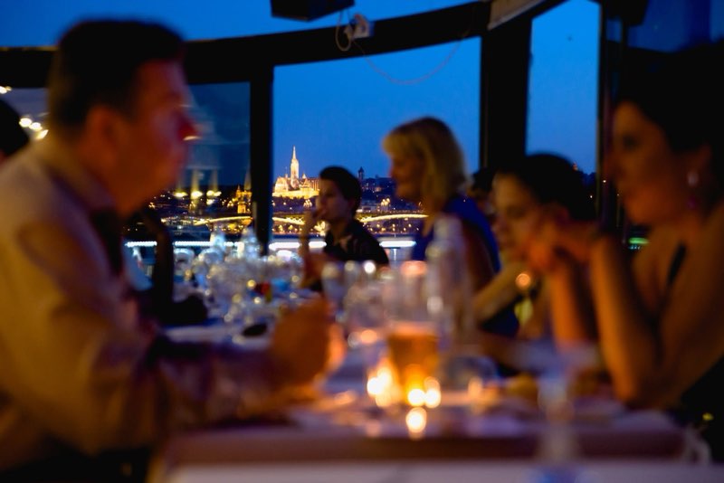 Vendégek a panorámás teraszon, háttérben a kivilágított budai oldal